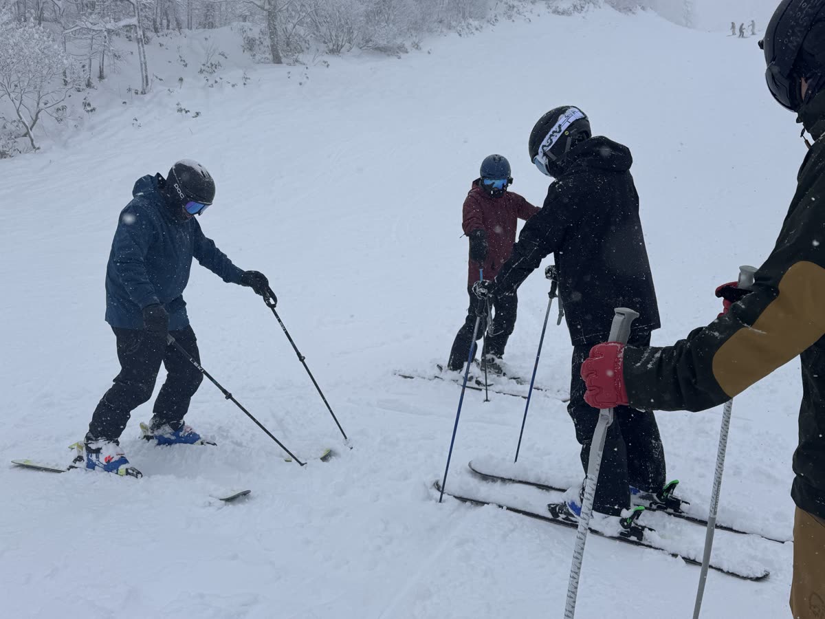 教練在飄雪的雪道示範雙板動作,學員在旁觀察