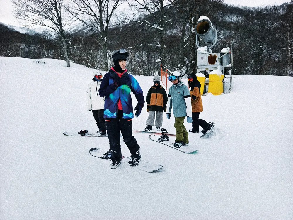 教練在雪道上，面對學員示範與講解單板動作
