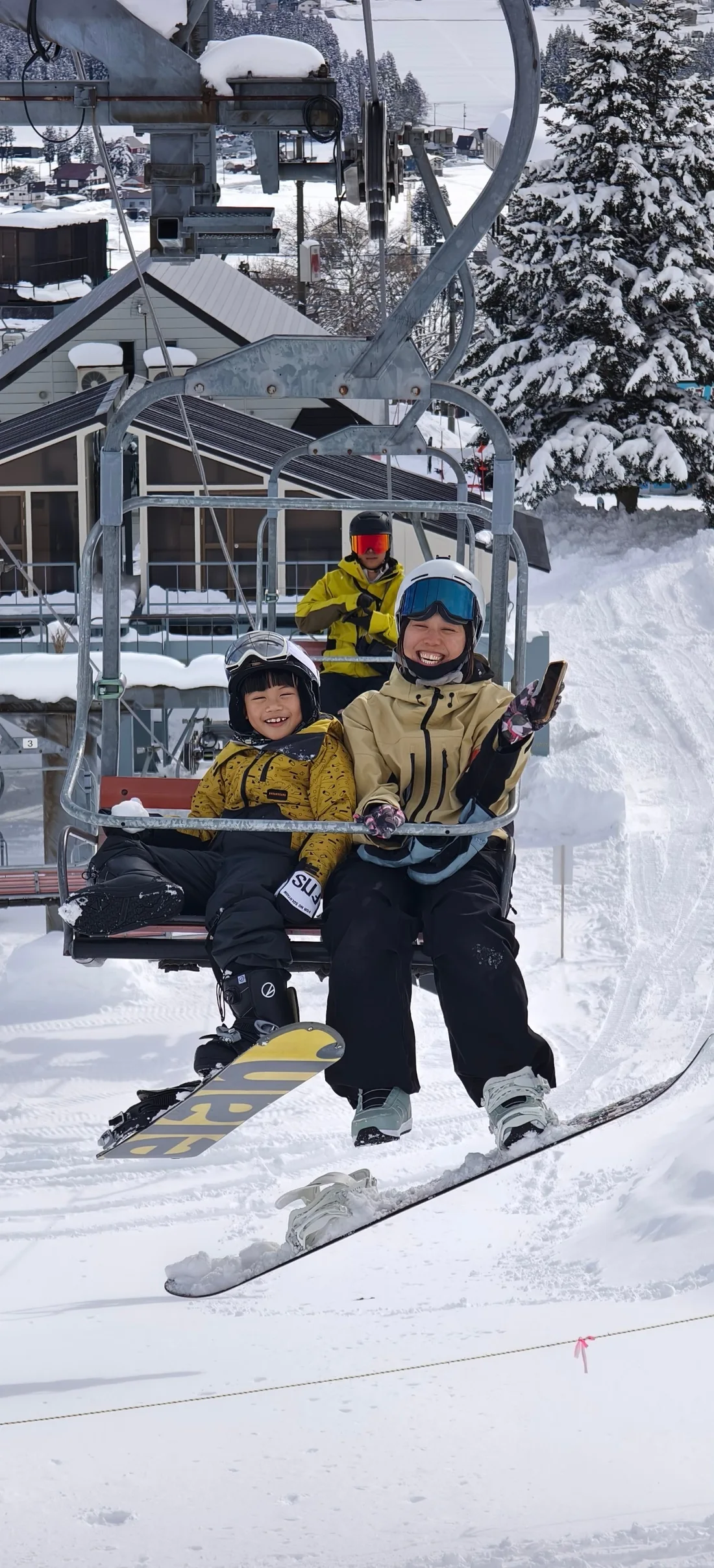 岩原雪場吊椅上,兩位戴著安全帽的滑行者並肩面向鏡頭微笑