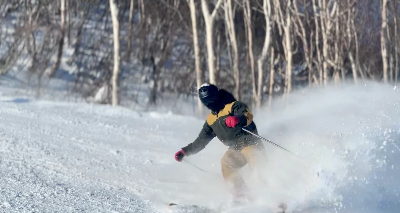 岩原雪場中,雙板滑行者在雪林旁轉彎,揚起雪花