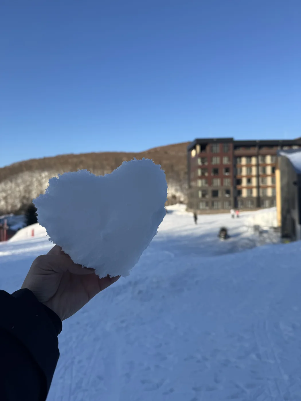 KIRORO 雪地裡,一隻手捧著心形雪塊,後方為山麓建築